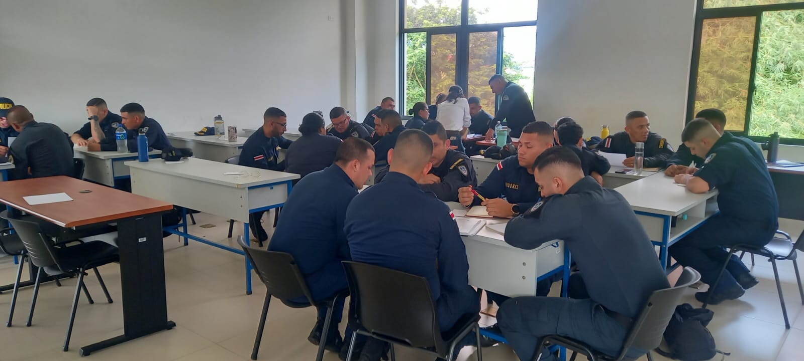 personas policías trabajando en grupos en un aula. Cada grupo está reunido en una mesa
